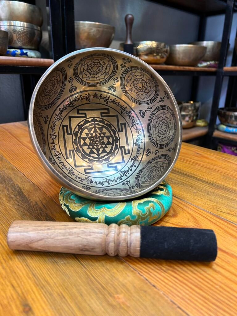 An engraved singing bowl on a green cushion with a wooden mallet.